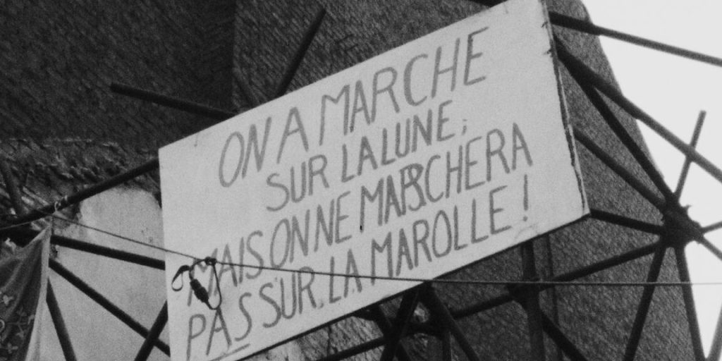 Gros plan sur une pancarte de la "Bataille des Marolles". Le texte écrit à la main dit : "On a marché sur la Lune mais on ne marchera pas sur la Marolle !"
